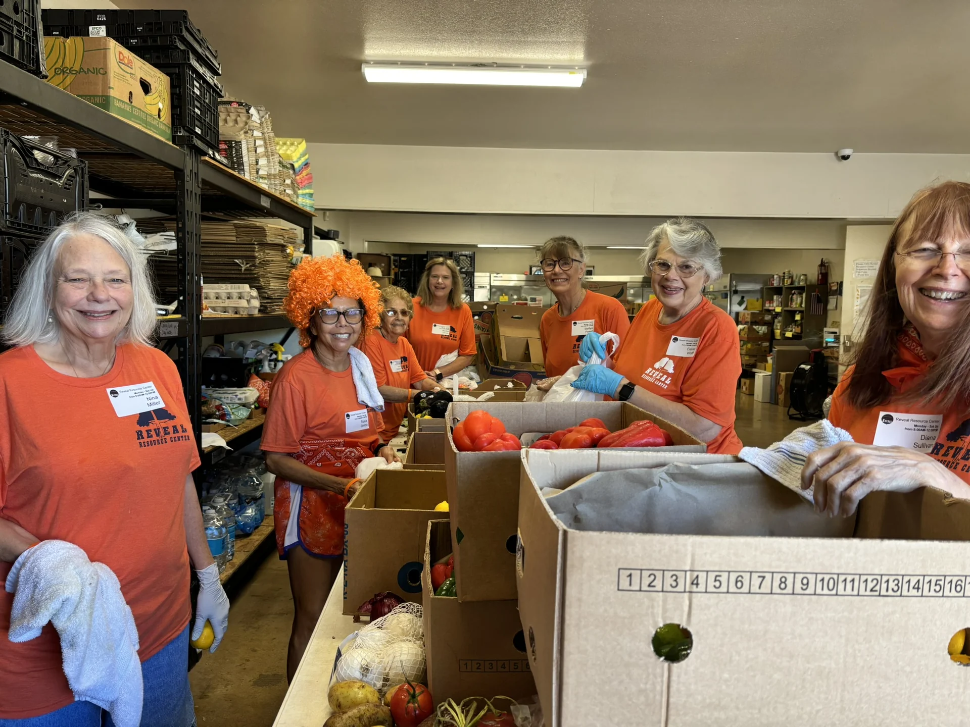 The full Reveal food-distribution volunteer group standing among fresh produce and pantry supplies.