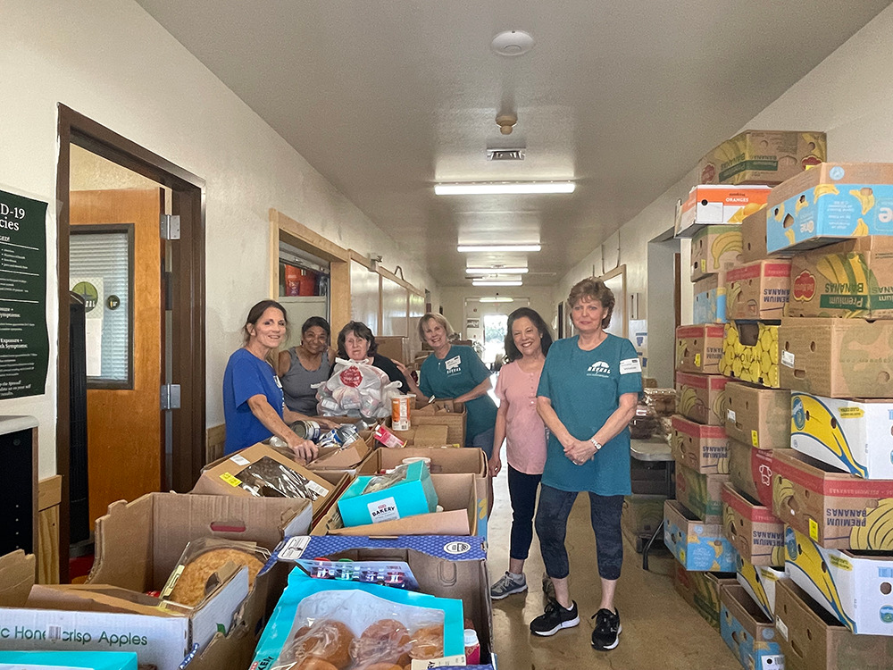 Reveal volunteers standing in a food-pantry sorting area with donated food.