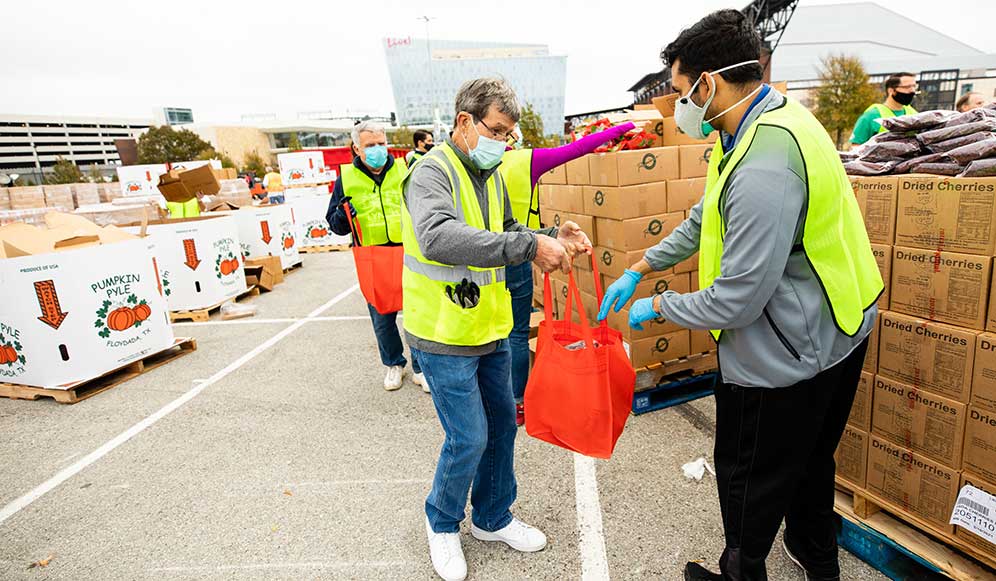 Reveal volunteers handing a food bag to a community member at an outdoor distribution.